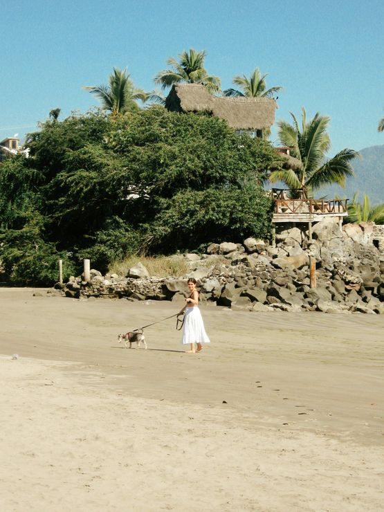 Woman in gray jacket, headphones, and watch, smiling in a park, surrounded by trees.