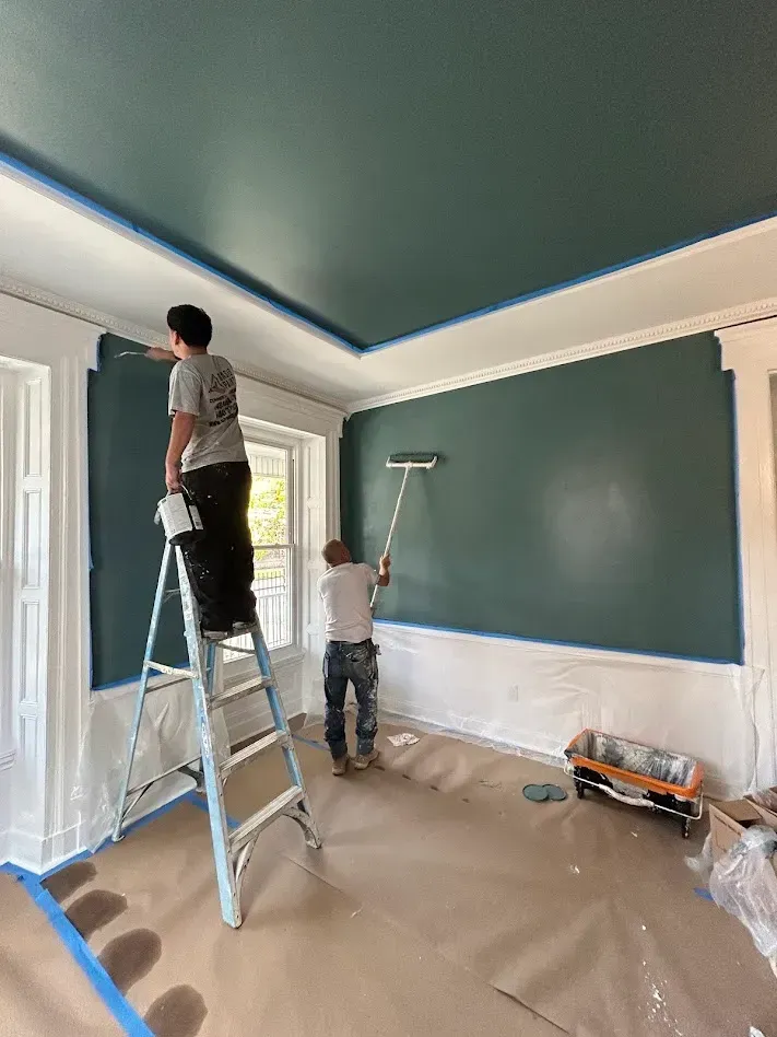 Two professional painters painting green interior walls in a home renovation project in Germantown, PA.