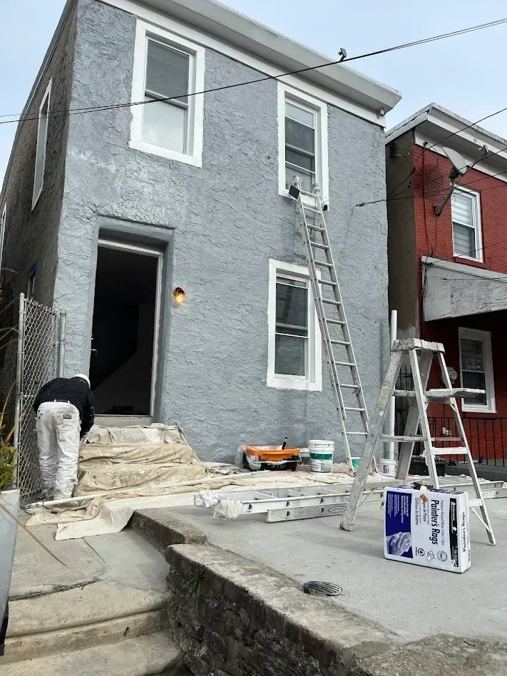 Exterior house painting in Germantown, PA with a professional painter using drop cloths and ladders.