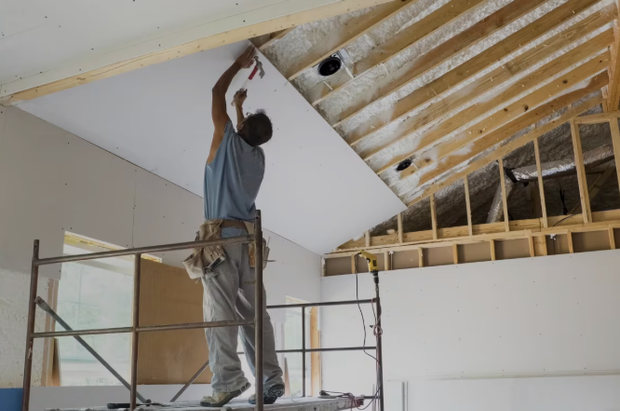 A man is standing on a scaffolding, working hanging a drywall
