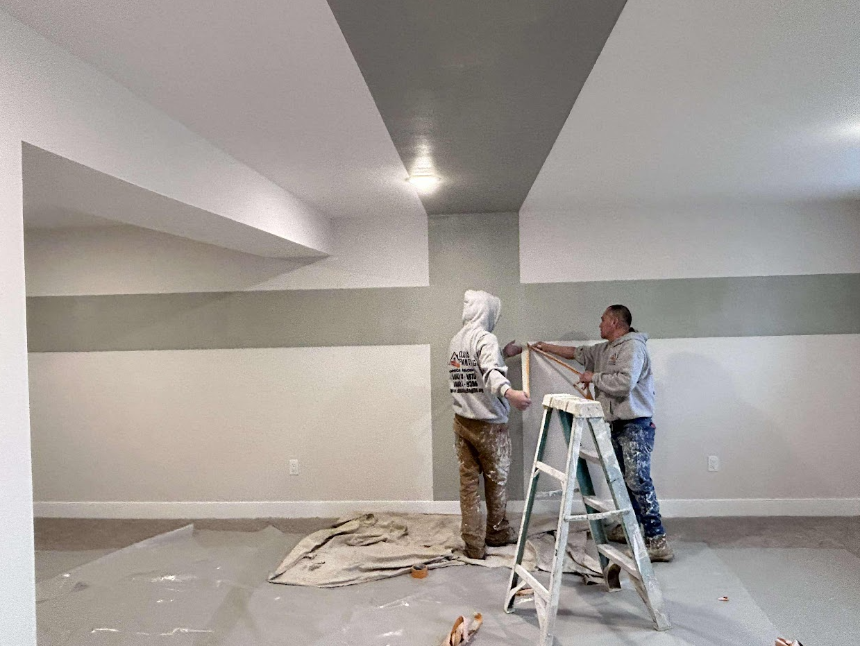 Two men are painting a wall in a room with a ladder in Chester County