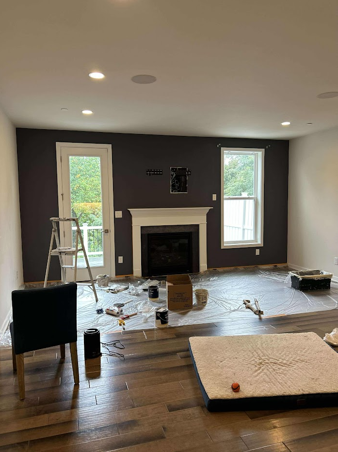 A living room with a fireplace and ladder is being painted black in West Chester County.