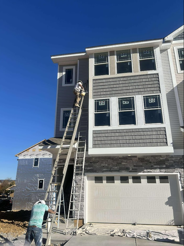 A man is painting the side of a house with a ladder.
