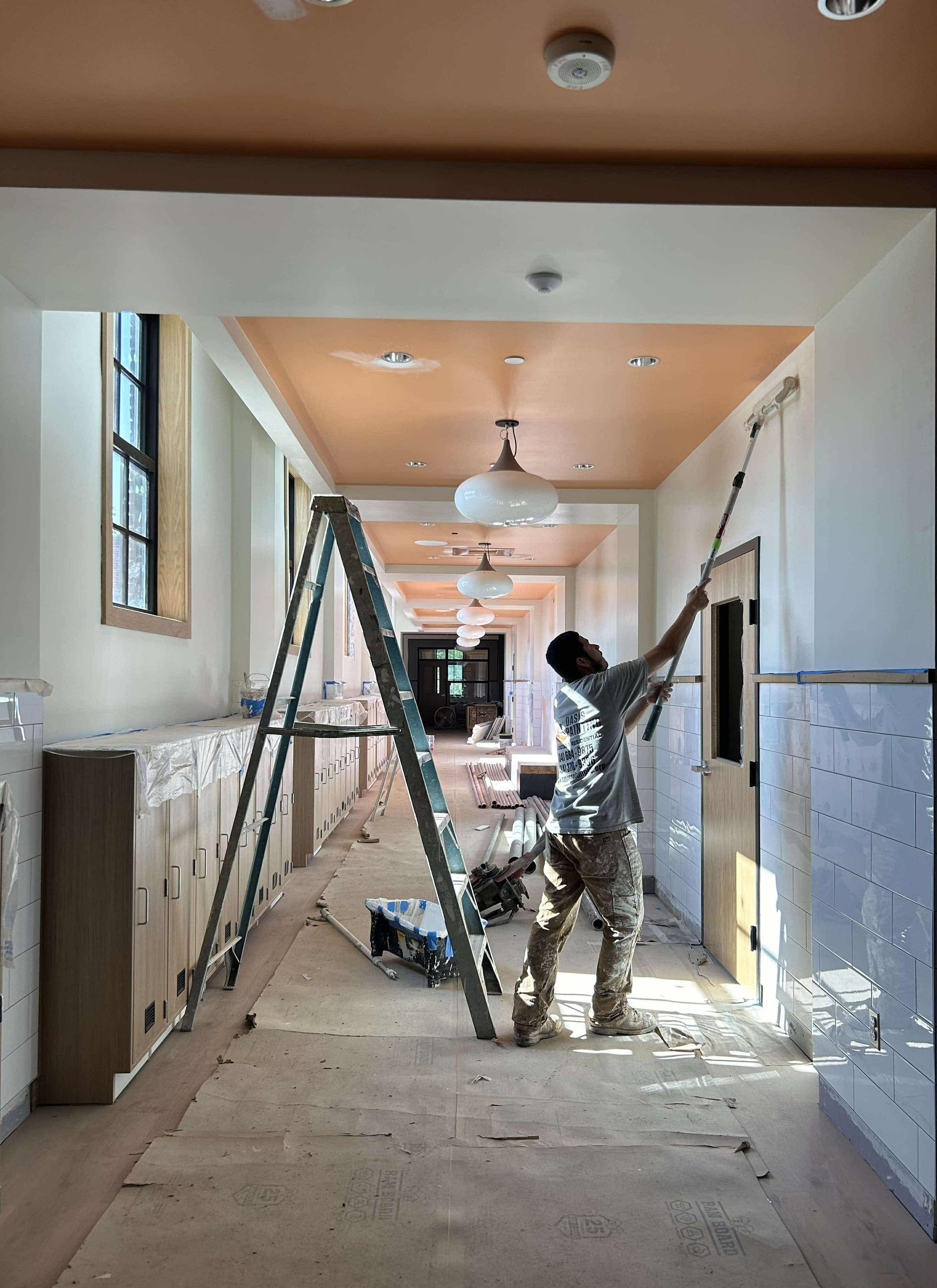A man is painting a wall in a hallway with a roller and a ceiling painted orange