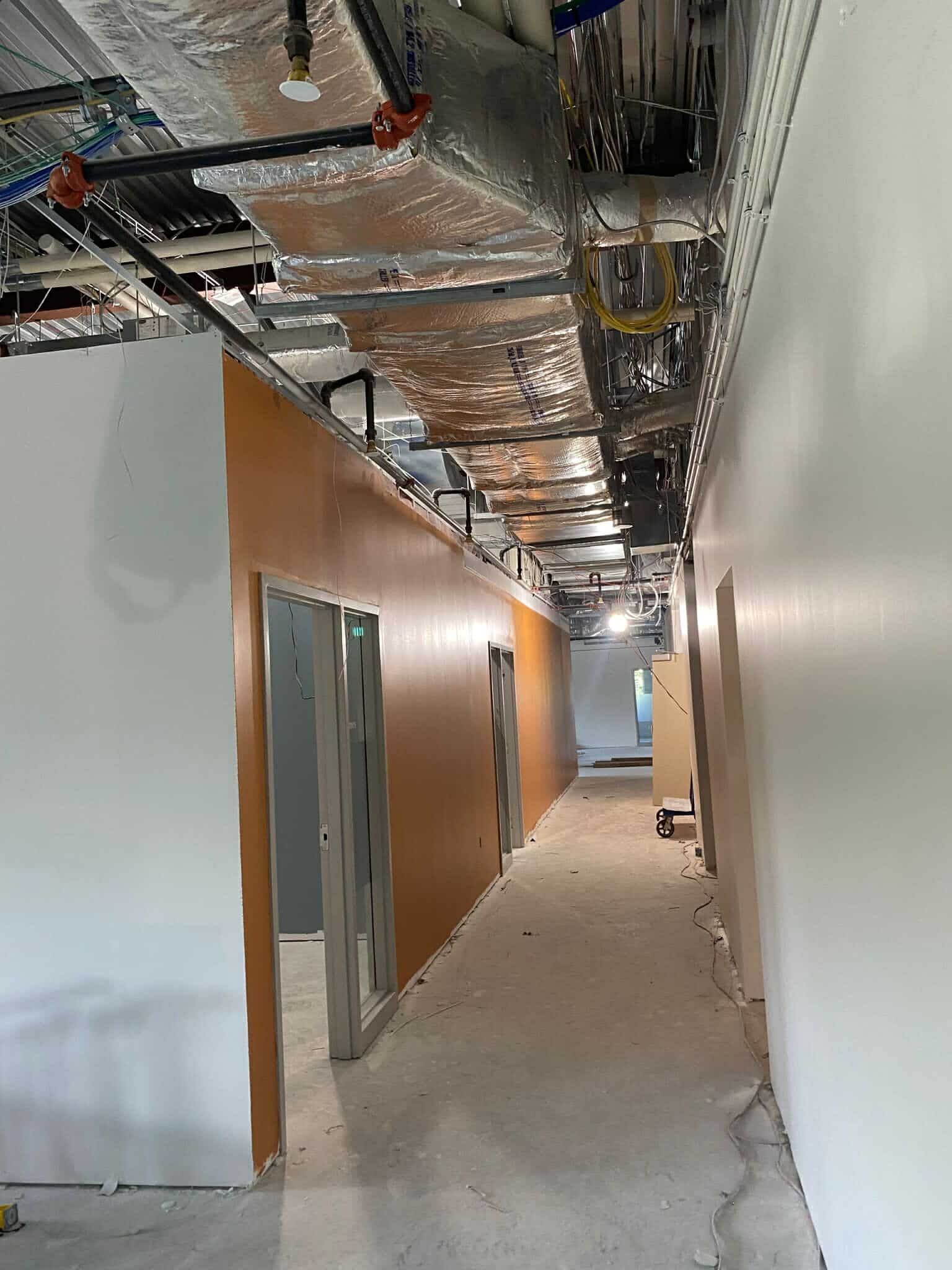 A long hallway painted orange on one side wall and white on the other wall in a building under construction.