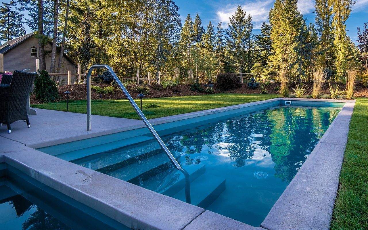 Rectangular pool with entry steps, handrail, and clear blue water, surrounded by green grass and trees.