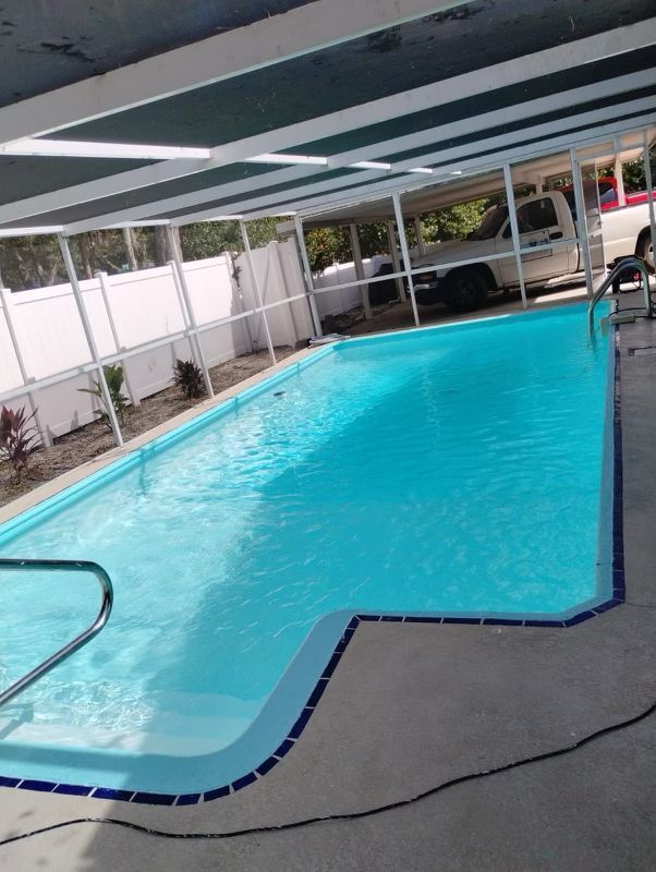 Rectangular pool with turquoise water under a screened enclosure. White fencing surrounds the pool area.
