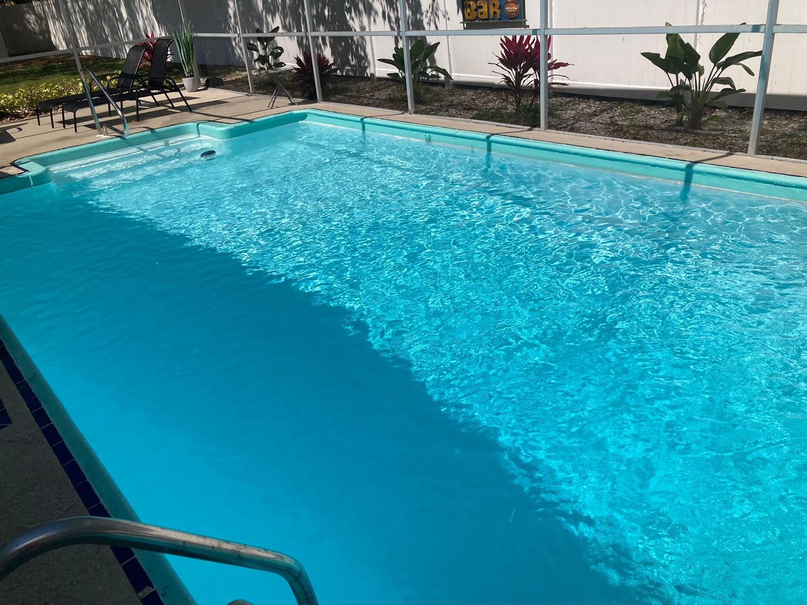 A rectangular swimming pool filled with turquoise water, with steps at one end and a handrail.