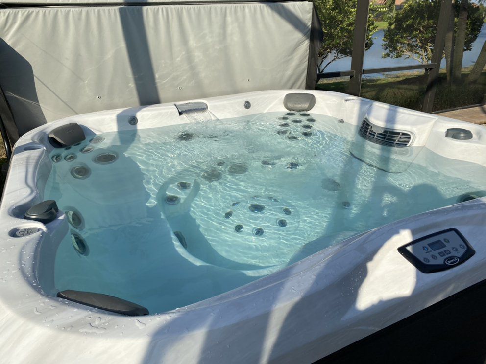 Hot tub filled with clear water, outdoors. White spa with jets and control panel.