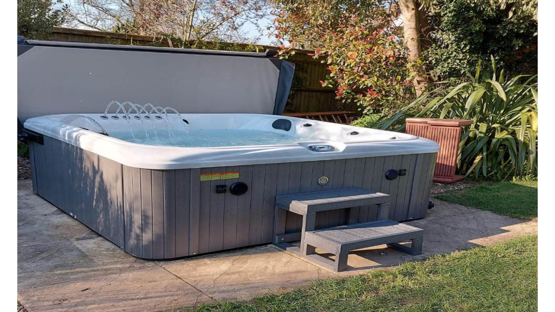 Gray hot tub with partially open cover, outdoor setting, gray steps.