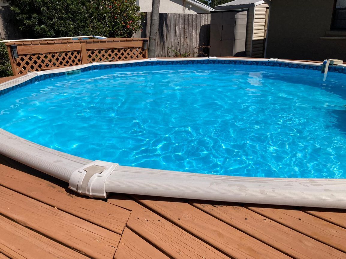 Above-ground swimming pool with blue water, surrounded by a wooden deck.