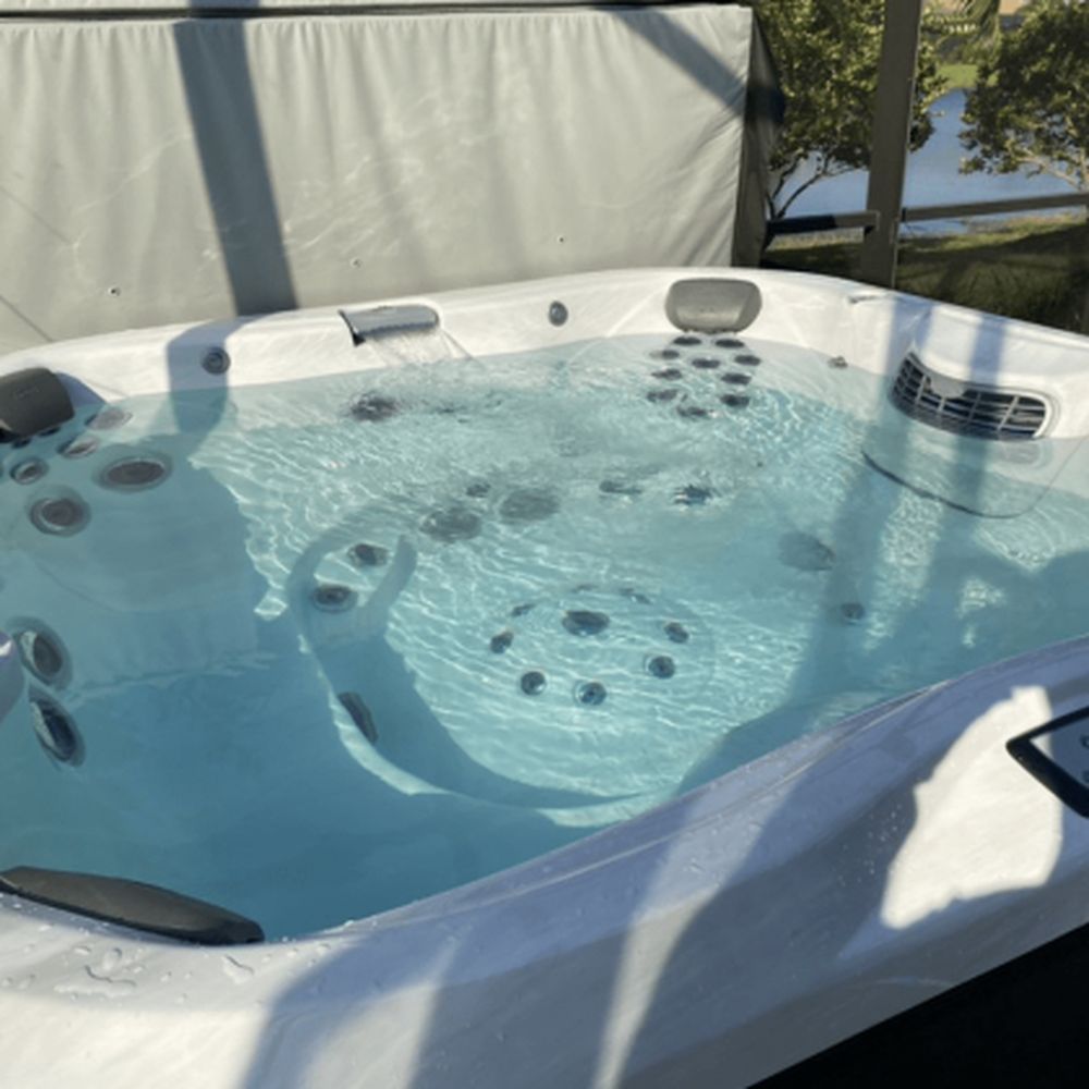 A hot tub filled with clear water, outdoors with a lake visible in the background.
