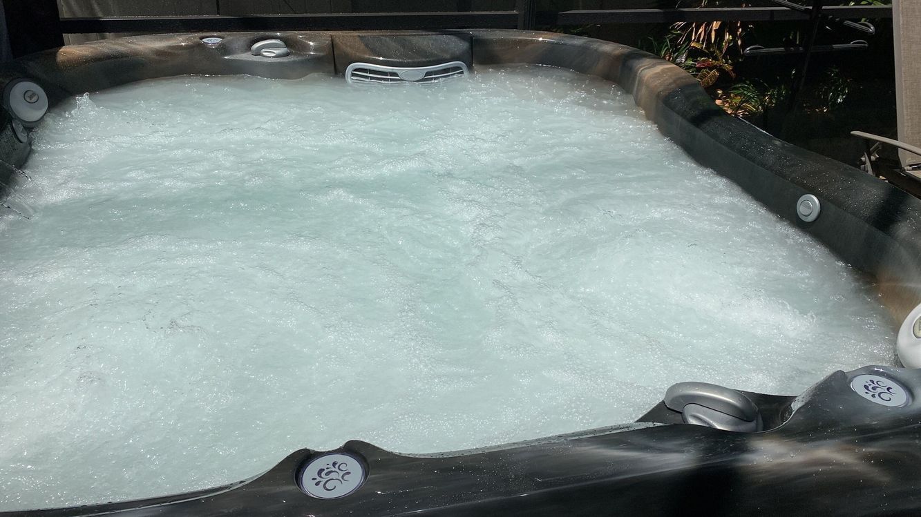 Bubbling hot tub with white water, black exterior, outdoors.