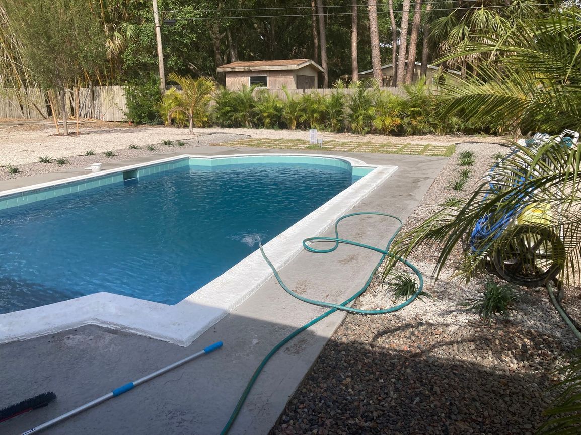 Pool with blue water and gray concrete surrounding it. Green hose on the right.