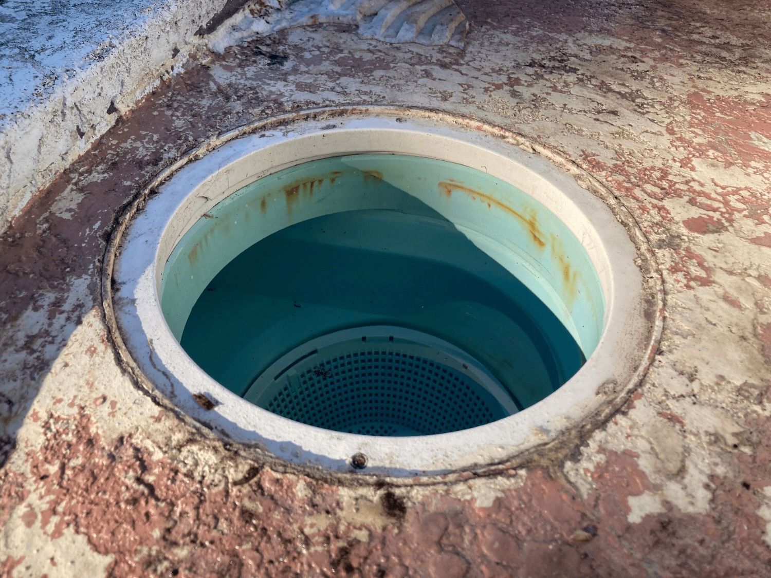 Open circular drain with blue water, surrounded by concrete.