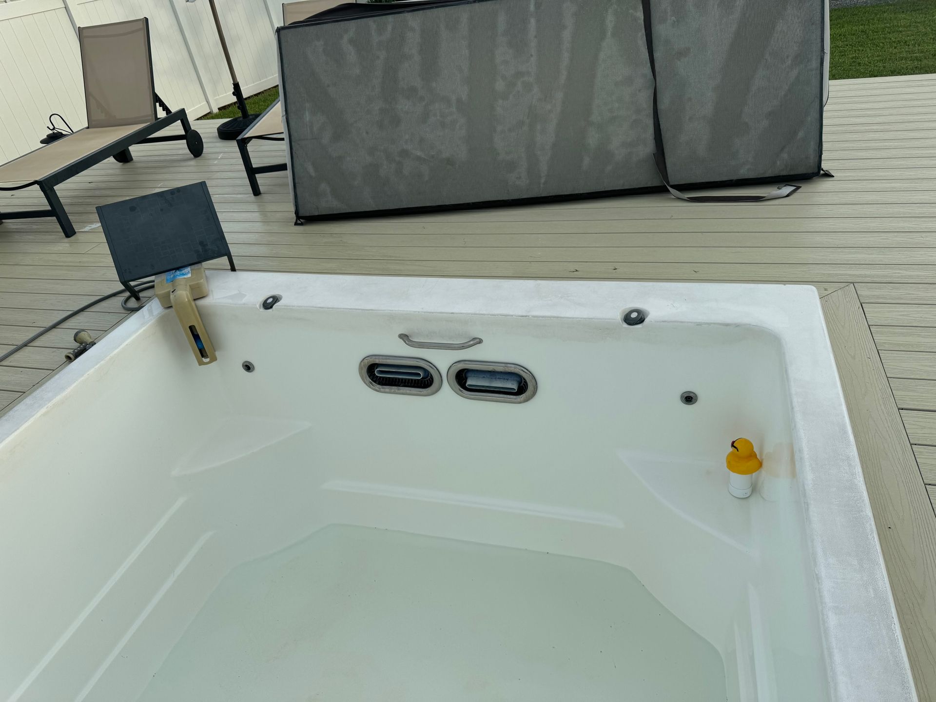 White hot tub on a wooden deck with a gray cover.