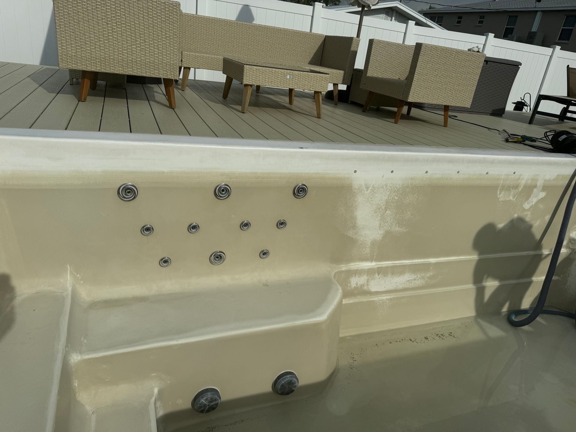 Hot tub with multiple jets, tan interior, on a wooden deck with beige patio furniture in the background.