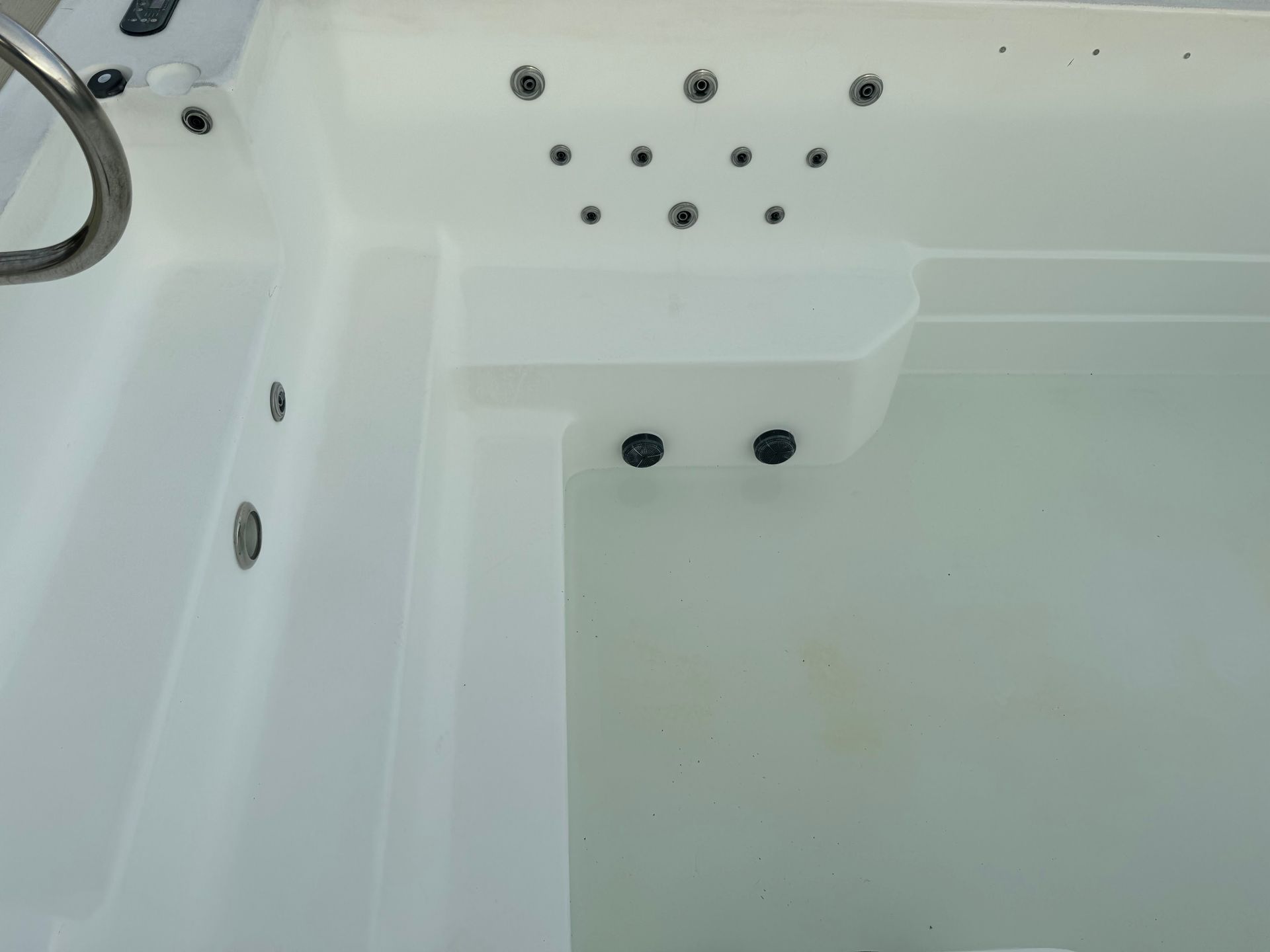Interior of a white hot tub with multiple jets, filled with clear water.