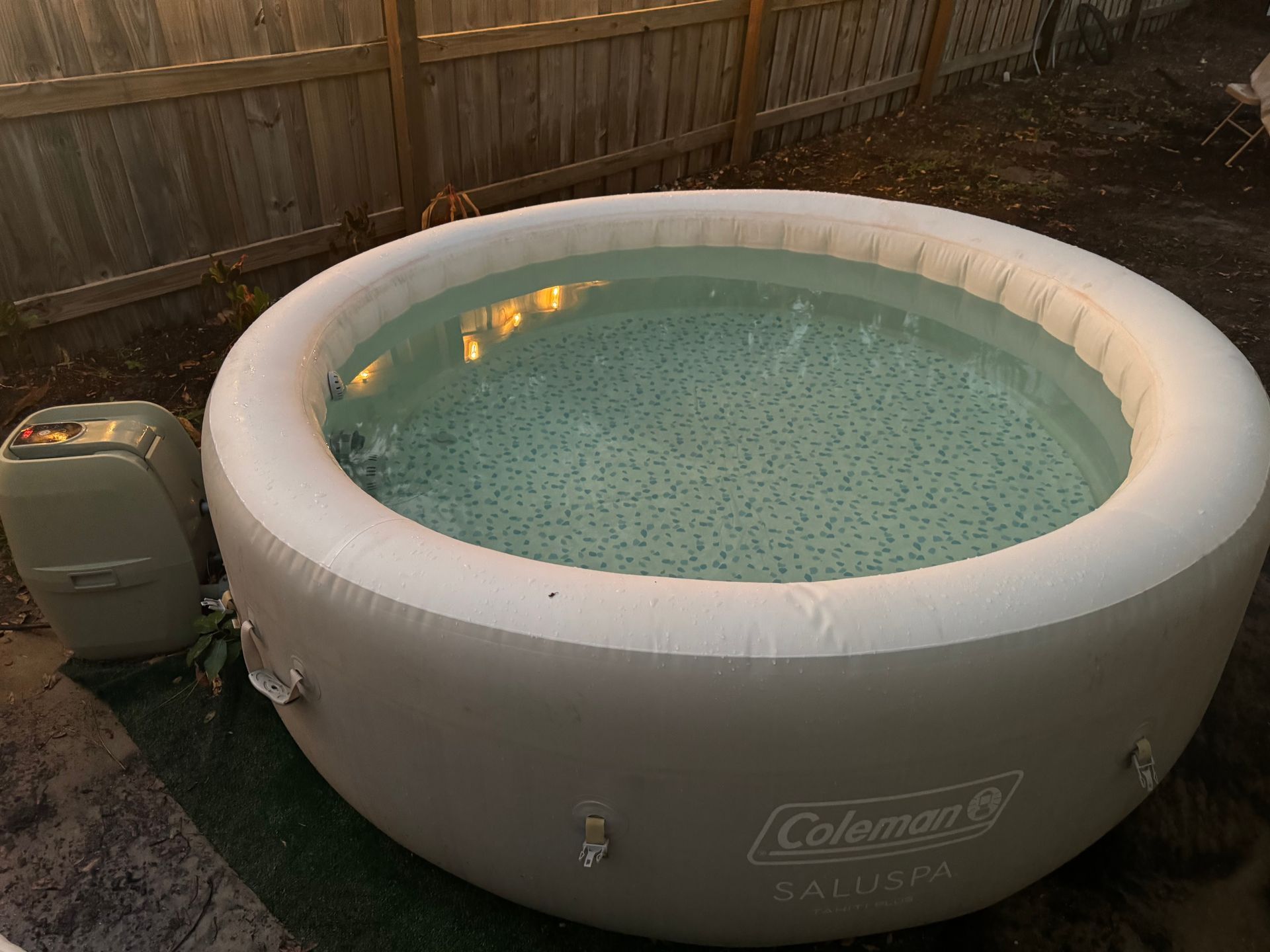 Inflatable Coleman SaluSpa hot tub filled with water, next to a power unit, outdoors at dusk.