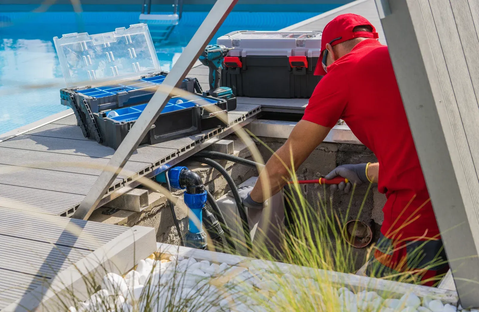 Man in red shirt repairing pool equipment next to the pool. Tools, open toolboxes.