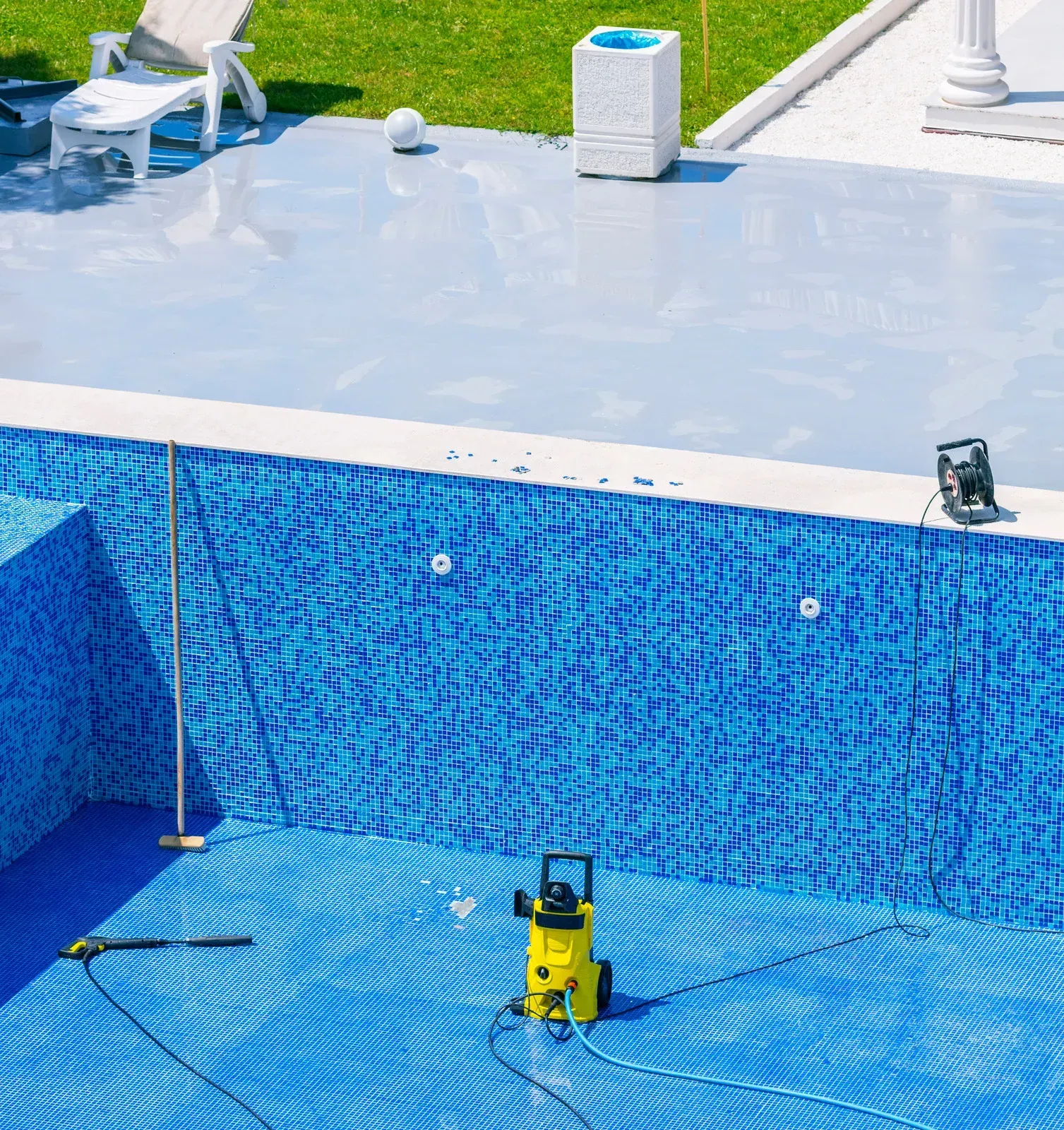 Pool being cleaned; blue tiled interior, a pressure washer, and tools are visible.