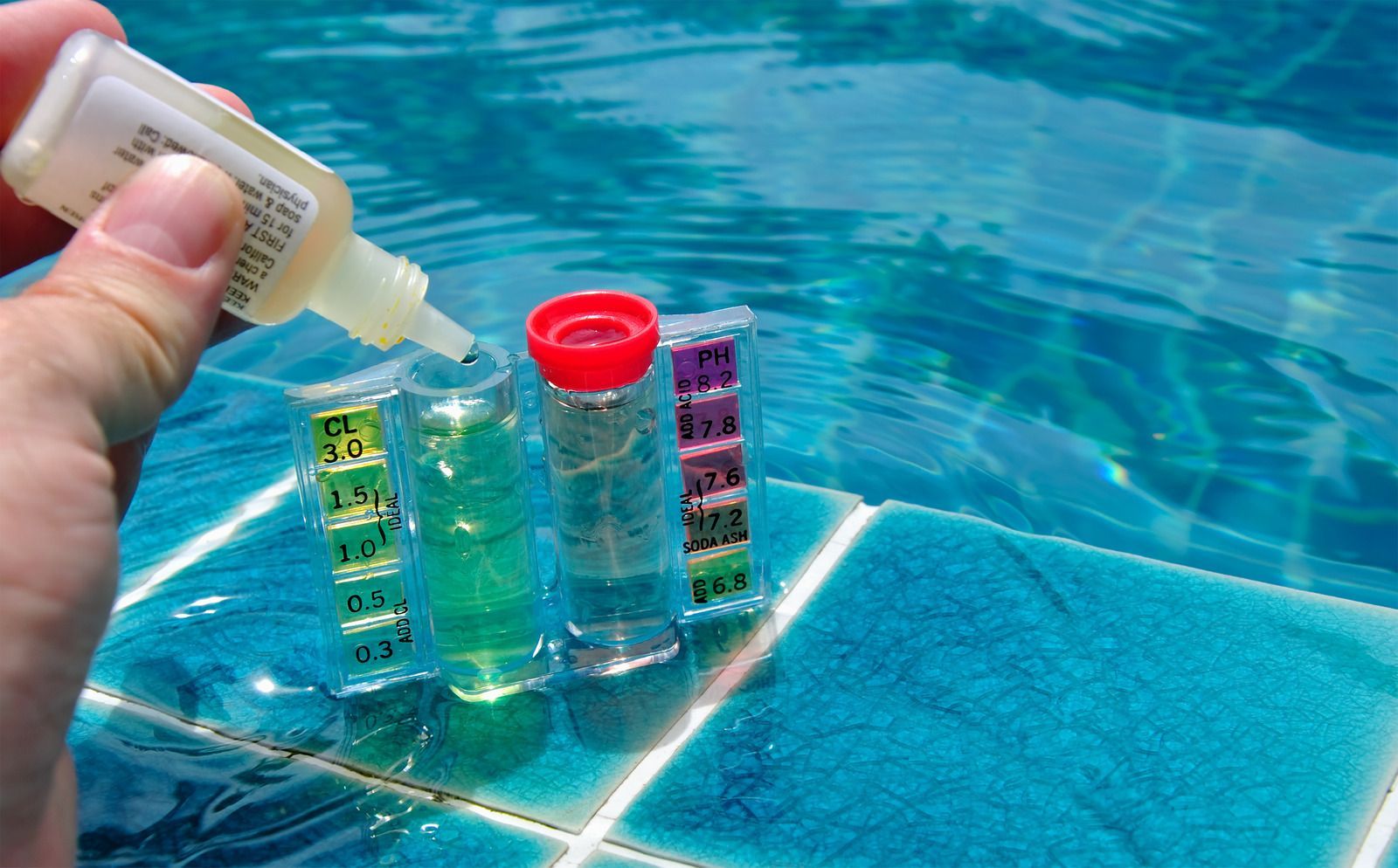 Person dripping liquid into pool water testing vials. Vials are on blue tiled surface.