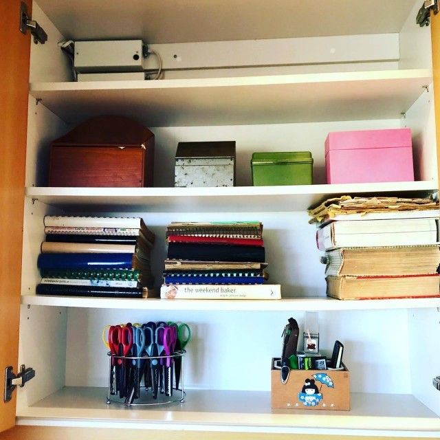 White cabinet with shelves. Boxes, books, notebooks, and scissors are organized inside.