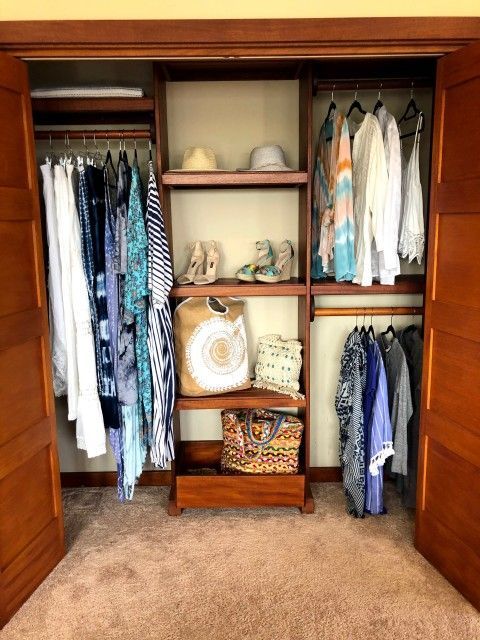 Wooden closet with clothes hanging, shelves with hats, shoes, and bags.