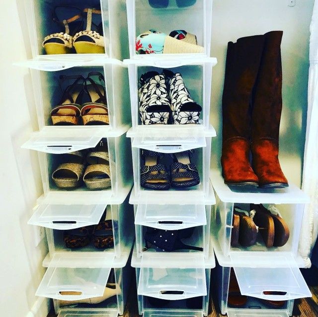 Shoes organized in clear plastic storage boxes in a closet.  Tall brown boots on the side.