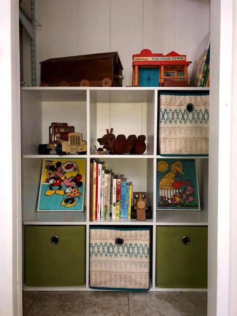 White shelving unit filled with toys and storage bins. Some bins are green; others are patterned.