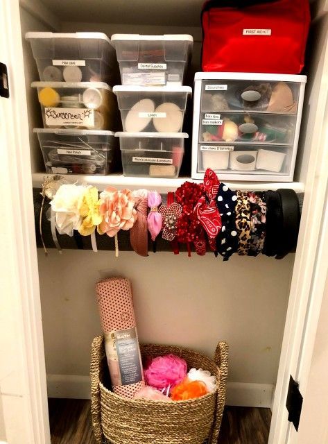 Closet organization with clear bins, red bag, accessories, and a basket holding a rolled item.