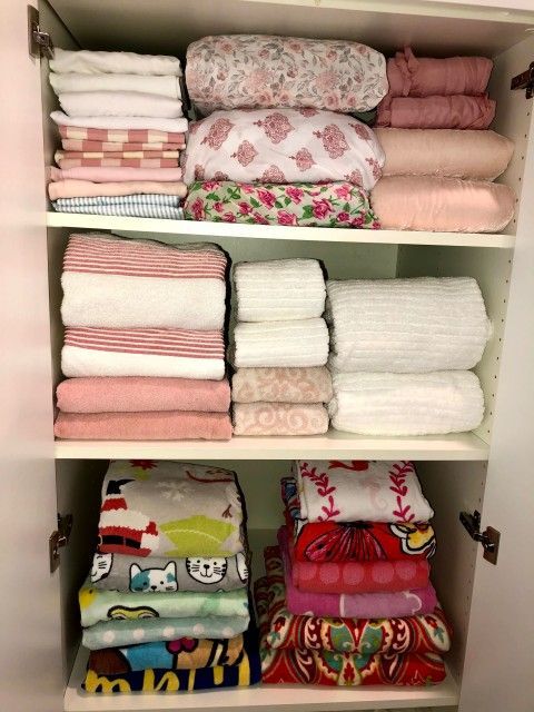 Closet organized with stacks of folded towels and bedding in various colors and patterns.