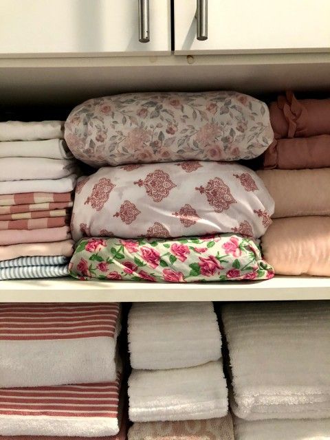 Shelves in a linen closet with neatly stacked bed linens and towels in various colors.