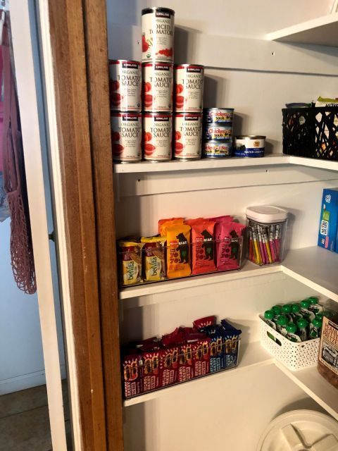 Pantry with canned tomatoes, tuna, snacks, and spices on white shelves.