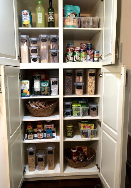 White pantry filled with organized food items in clear containers, baskets, and on shelves.