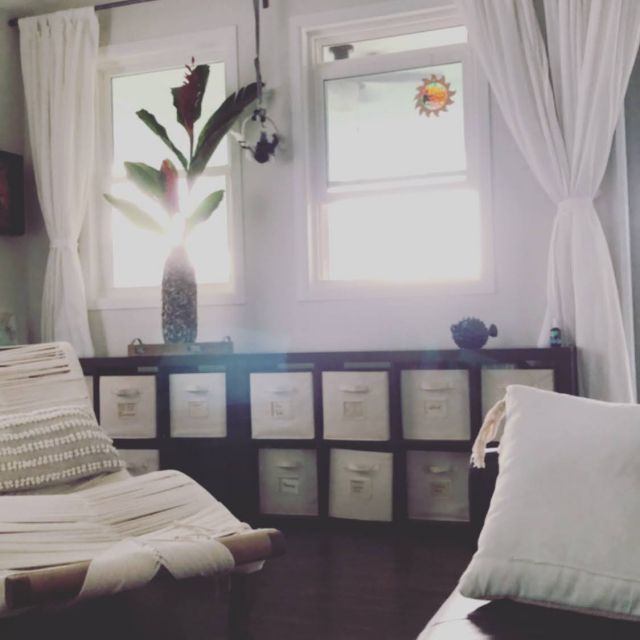 Bright living room with sunlight streaming through windows, sheer curtains, storage unit, and cozy seating.