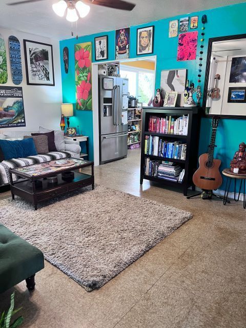 Living room with teal walls, bookshelves, and a rug. Guitar, artwork, and a sofa are visible.