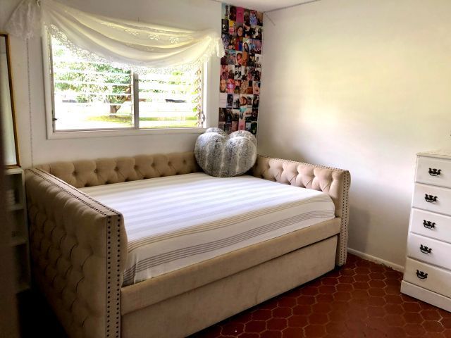 Beige daybed in a room with a window, white dresser, and patterned floor. A heart-shaped pillow sits on the bed.