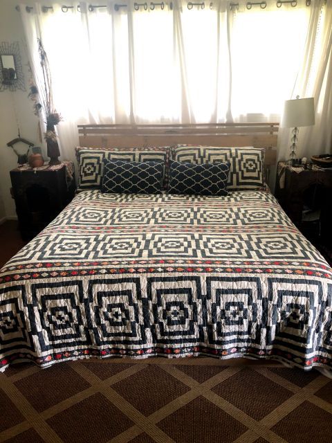 Bedroom with bed covered in patterned quilt, pillows. Wood headboard.