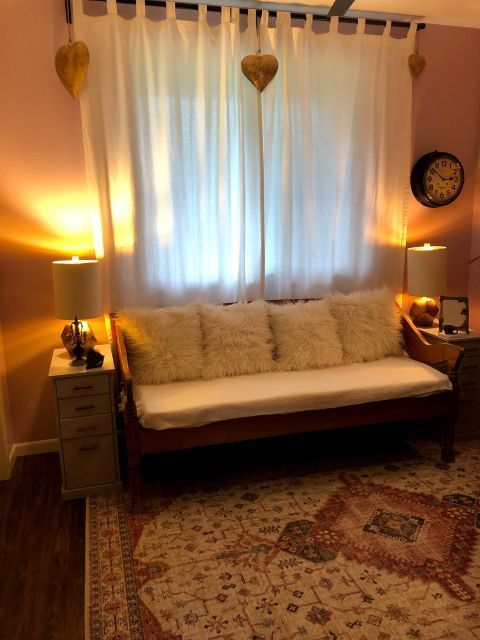 Room with a daybed, white curtains, pink walls, and a patterned rug.