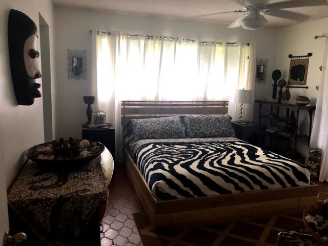 Bedroom with zebra-print bedding, wooden furniture, artwork, and white curtains.