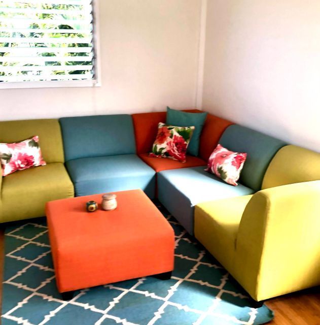 Colorful sectional sofa in a corner with an orange ottoman and floral pillows, on a teal rug.