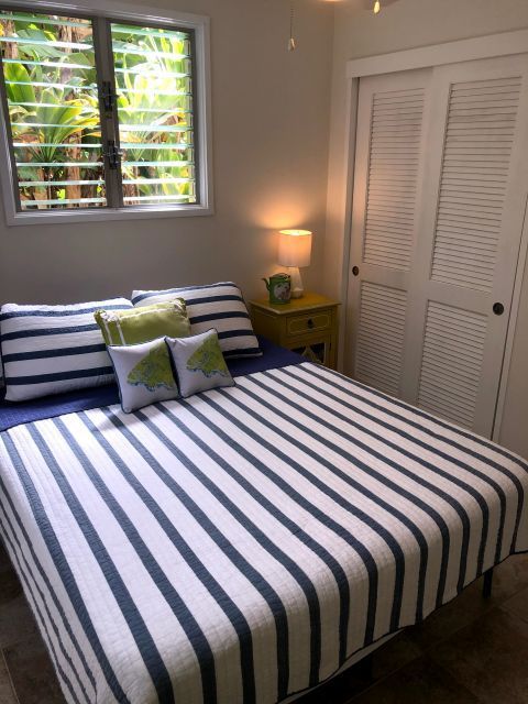 Bedroom with a blue and white striped bedspread, pillows, bedside table, and window.