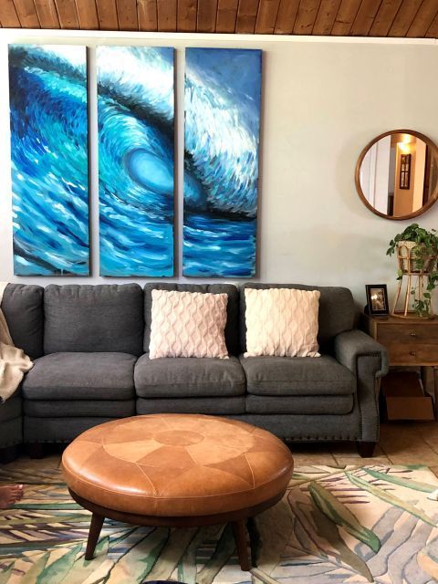 Living room with blue wave art above a gray couch, a round leather ottoman, and a leafy rug.