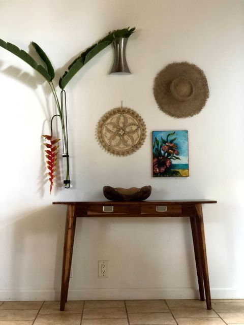 Wooden console table with wall decor of plants, hat, artwork.