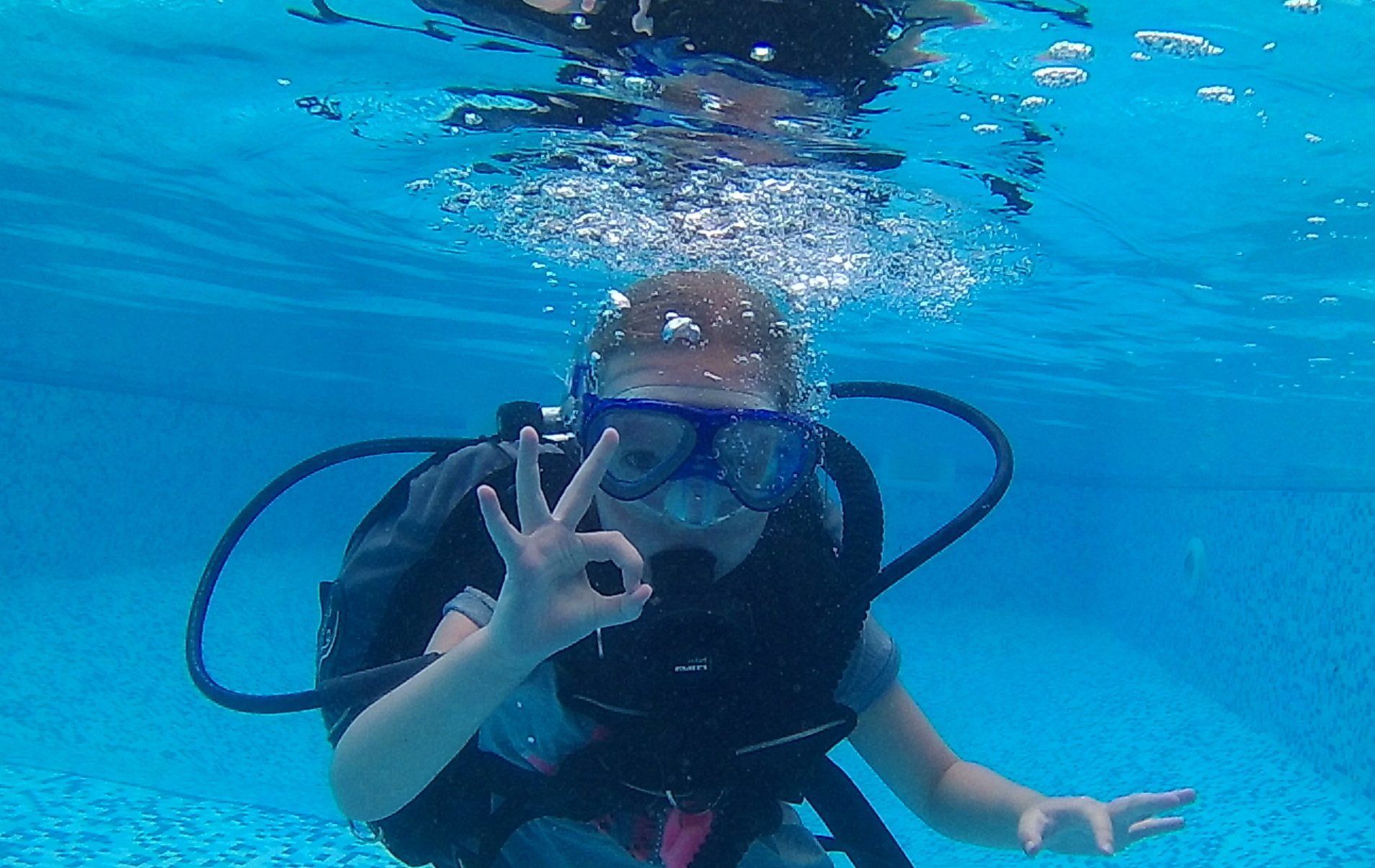 a child underwater with scuba gear making a hand symbol for ok