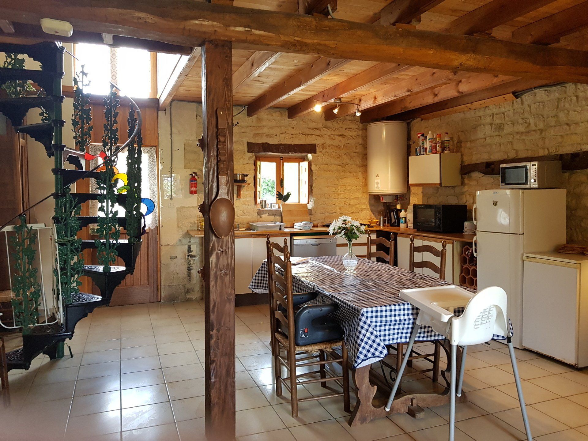 cuisine de campagne ouverte avec murs en pierres apparentes, nappe à carreaux bleus et chaise haute blanche Ikea