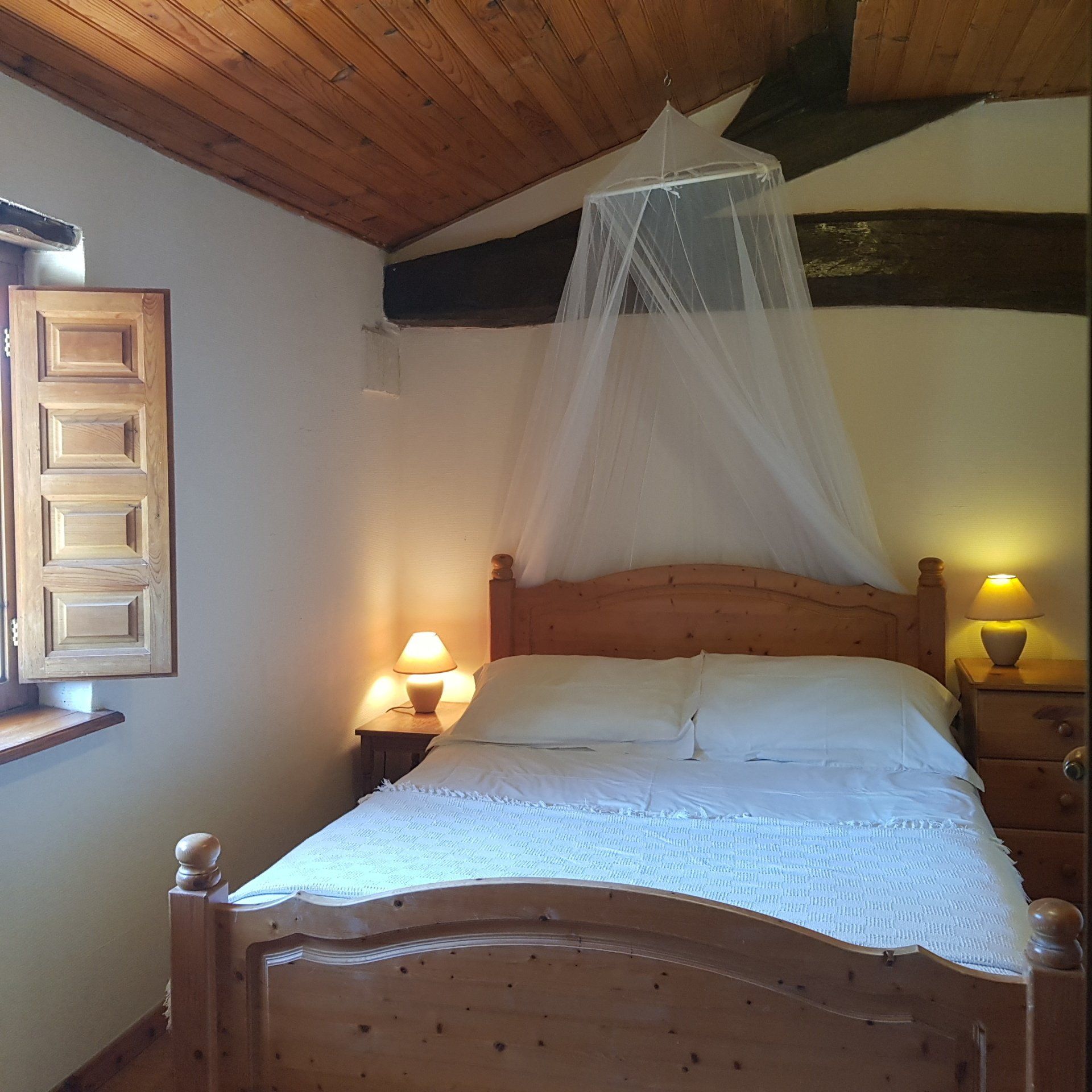 Pine wooden double bed with white linen and a white mosquitoe net above