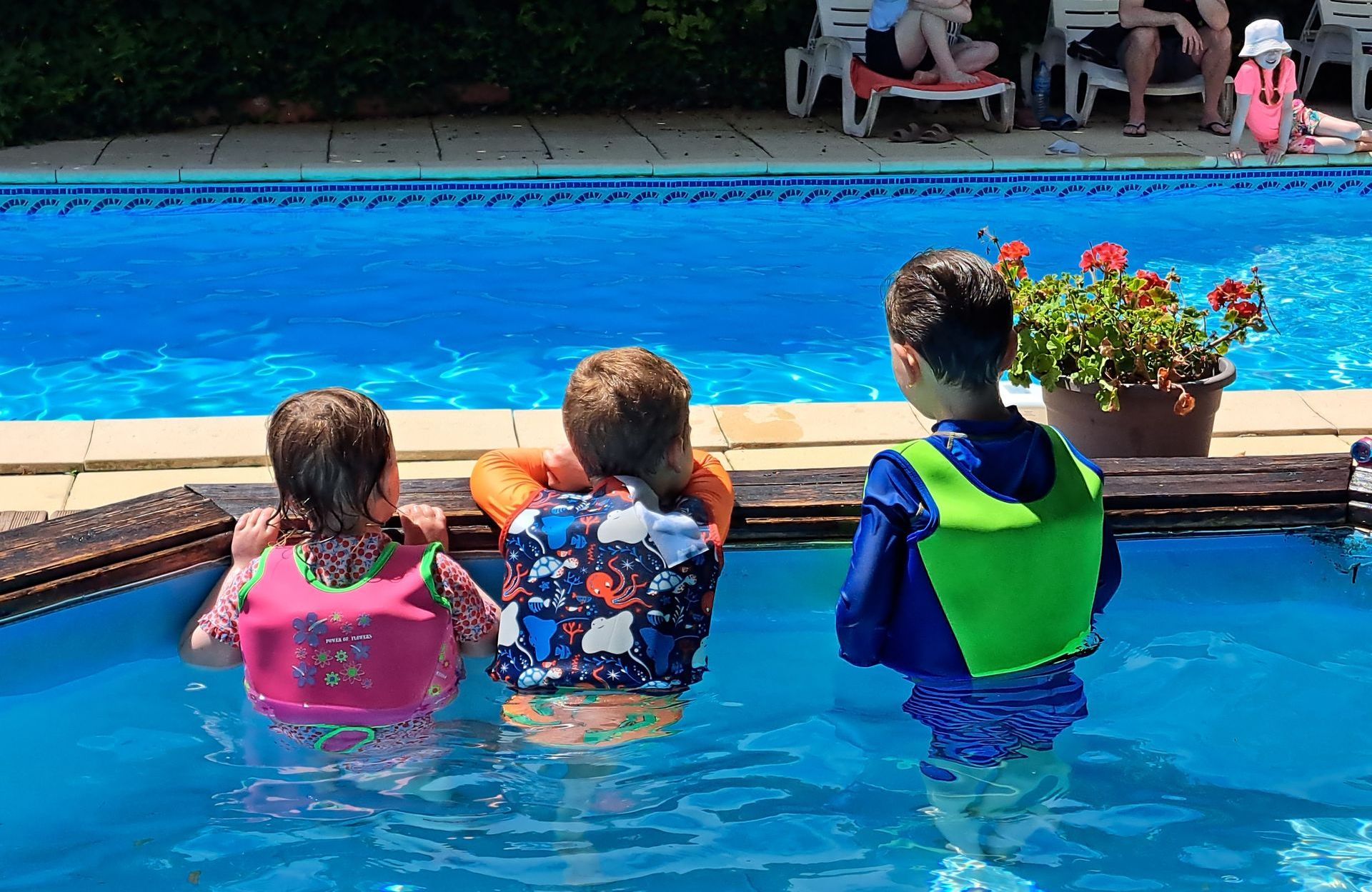 three children in a shallow pool looking at a big swimming pool