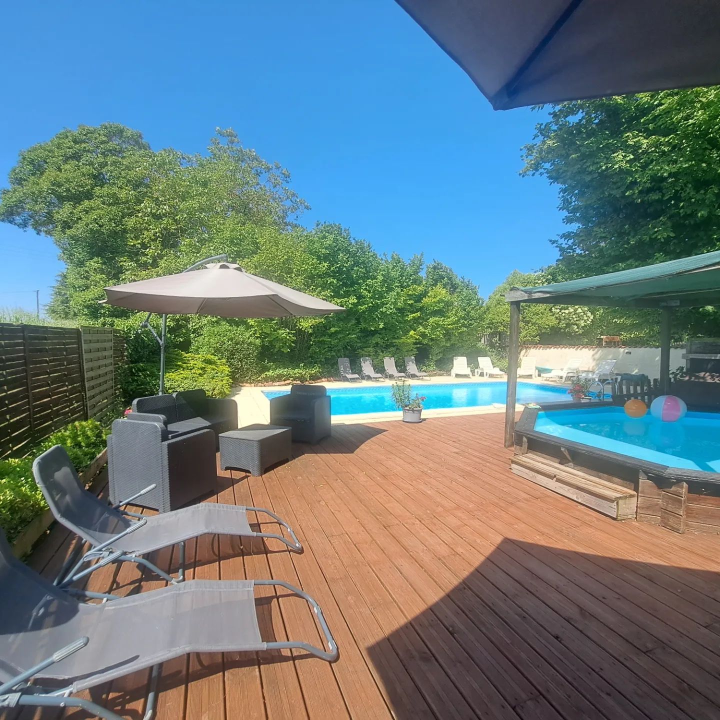 wooden sunbathring deck surrounding a toddler pool with big inground pool in background